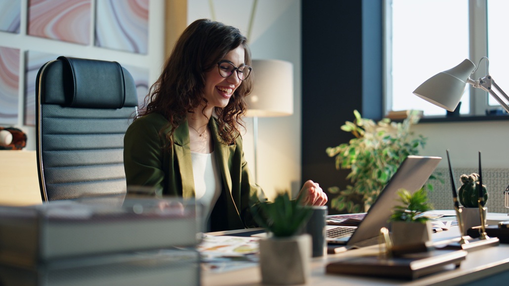 Excited businesswoman talking at video call sitting desk modern office closeup. Happy smiling girl manager satisfied by making successful deal speaking with partners in online conference. Work success